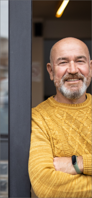 Image d’un homme souriant en pull orange avec les bras croisés sur le pas d’une porte